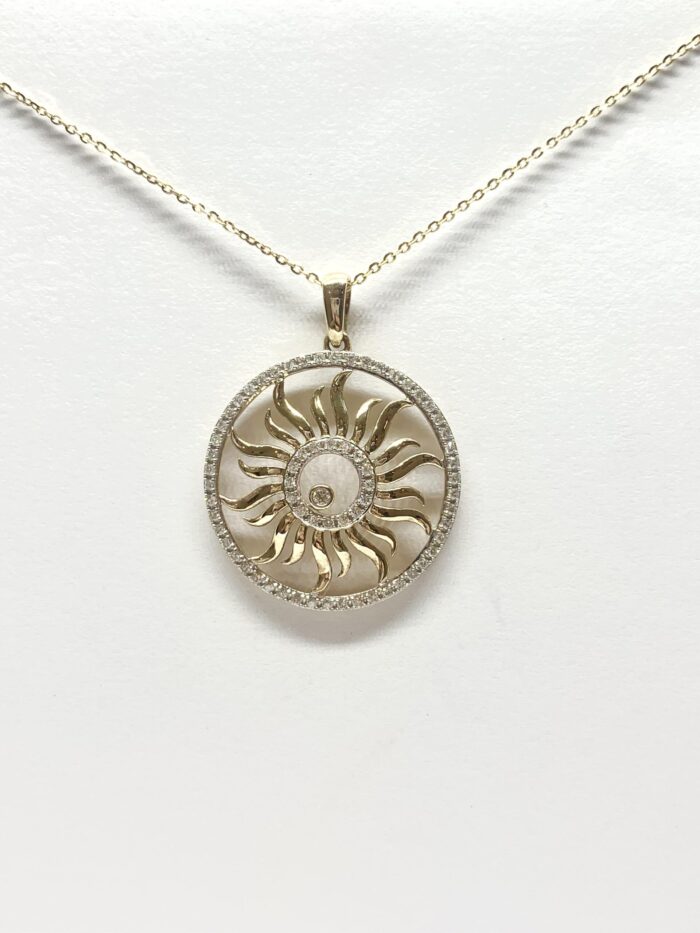 Gold pendant with a sunburst design, encircled by diamonds, on a delicate chain against a white background.