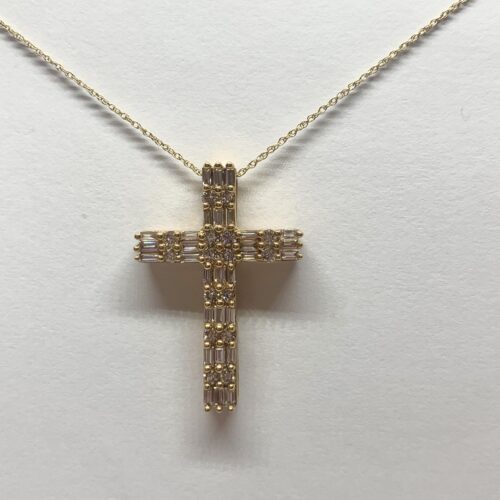 A close-up photo of a delicate gold cross necklace with sparkling diamonds, set against a soft white background.