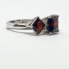 Elegant ring with three large, square-cut garnet stones set in silver, on a white background.