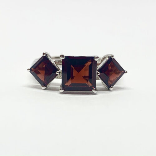 Elegant ring with three large, square-cut garnet stones set in silver, on a white background.