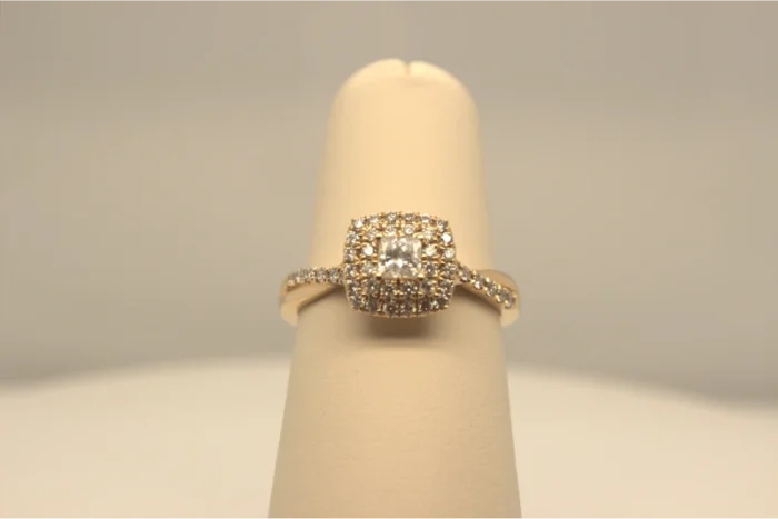 A cushion cut diamond engagement ring displayed on a light beige stand.