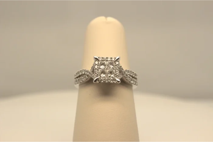An image of a princess cut diamond engagement ring on a beige ring stand.