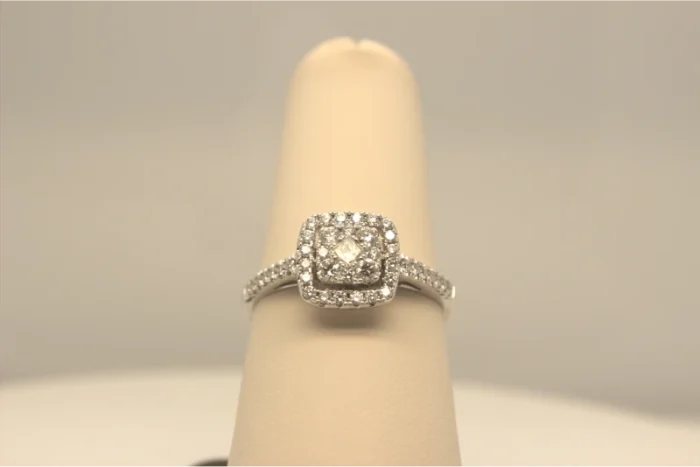 A diamond engagement ring with a cushion halo setting on a cream ring stand.