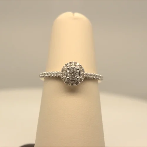 A diamond ring with a detailed halo setting, displayed on a light beige ring holder.